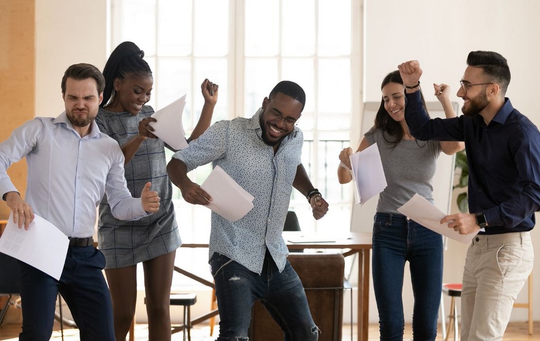 Fünf Menschen in einem Büro, die gemeinsam tanzen und sich freuen  