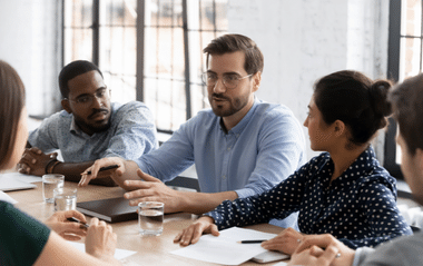 A group of people at a desk and talking animatedly 