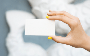 Eine Person mit gelben Fingernägeln hält eine weiße Karte hoch 